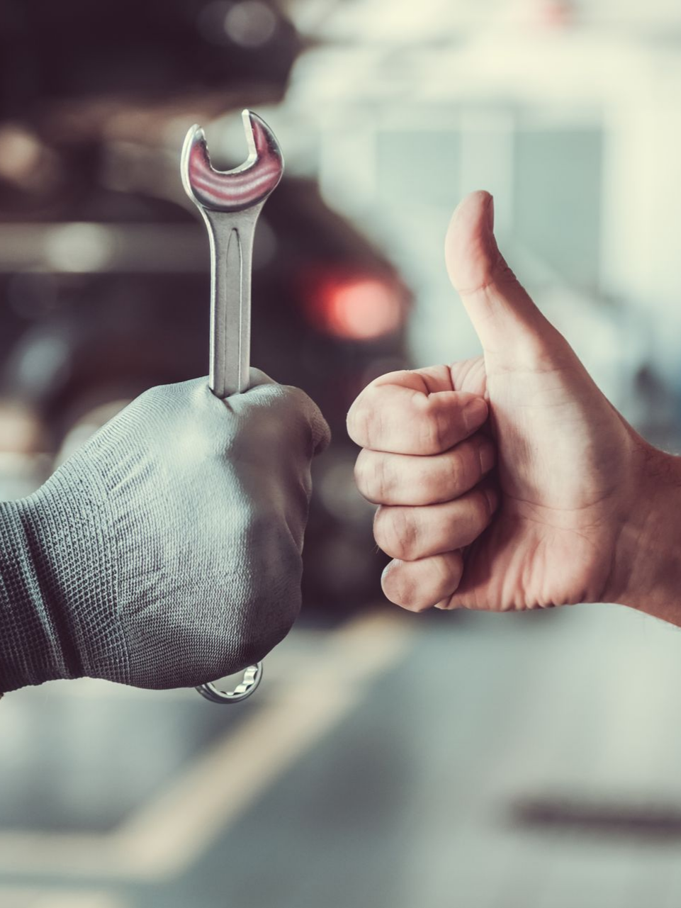 Dans un garage, une main gantée tient une clé à molette, tandis qu'une autre lève le pouce.