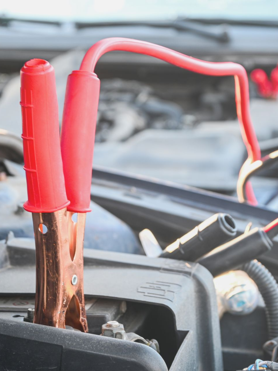 Des câbles de démarrage rouges et noirs connectés à une batterie de voiture dans le compartiment moteur.
