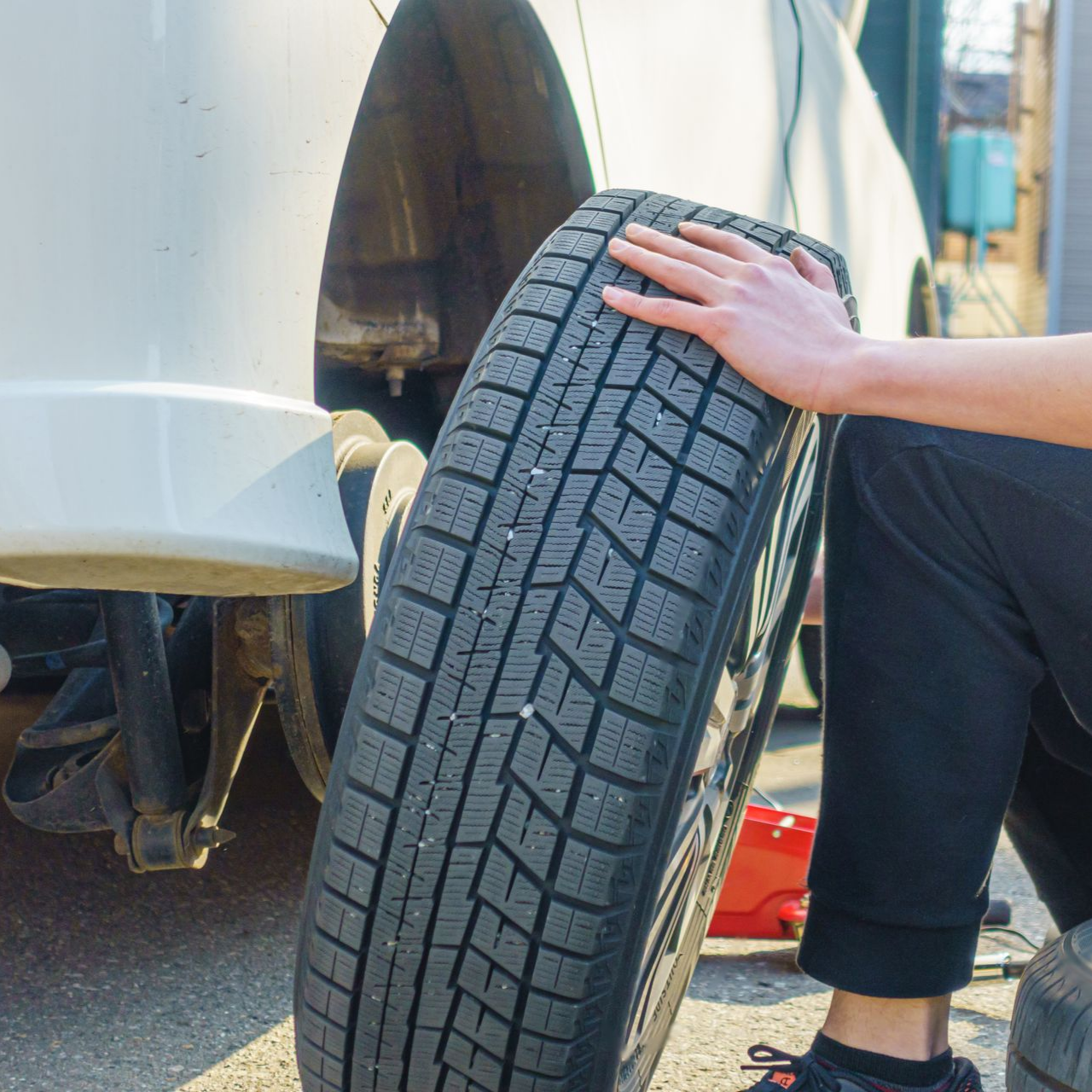 Une personne tient un pneu à côté d'un véhicule blanc.