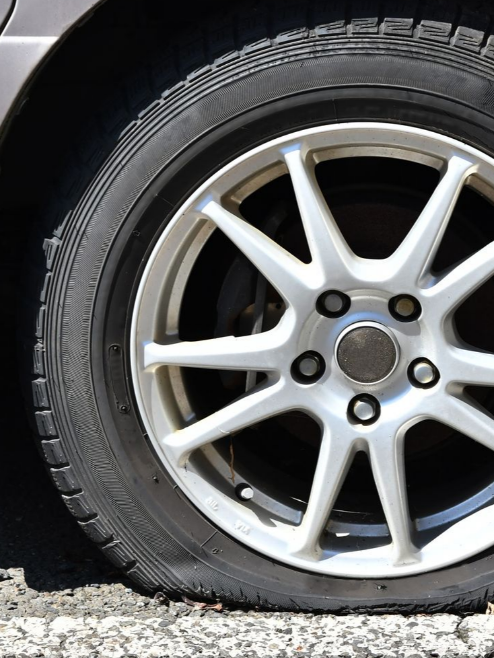 Un pneu de voiture dégonflé sur une surface asphaltée, avec une jante blanche et un pneu foncé, en extérieur.