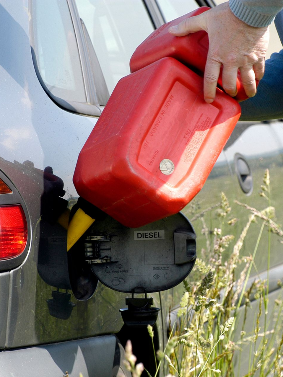 Une personne verse du carburant d'un bidon rouge dans le réservoir diesel d'une voiture.