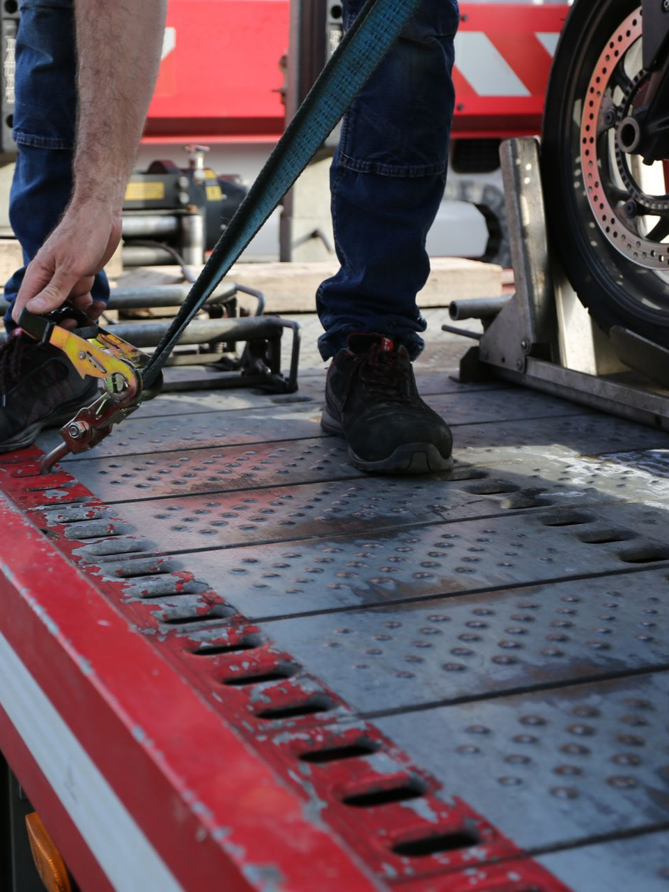 Une personne arrime une moto avec une sangle sur le plateau d'une dépanneuse.