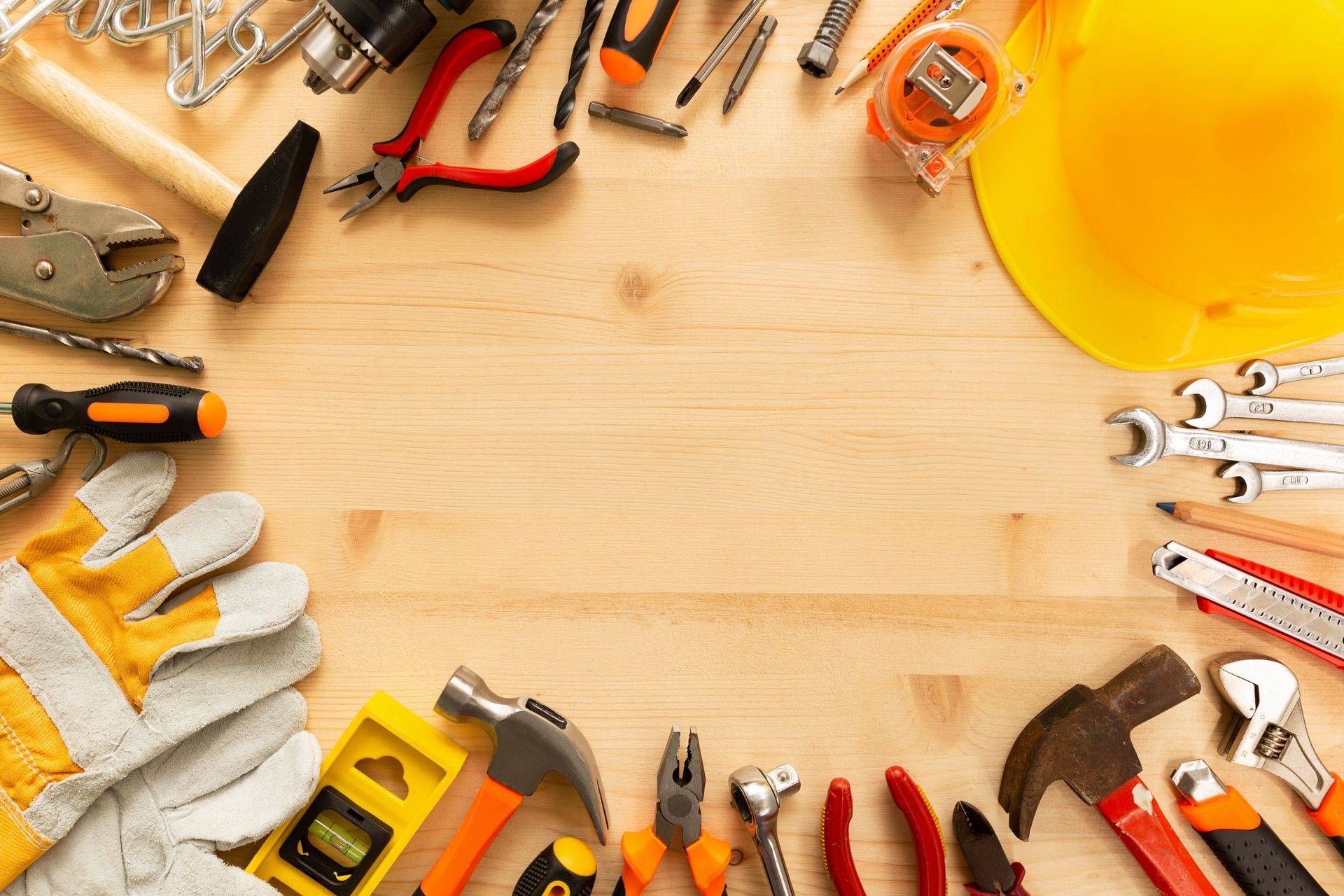 Outils à main et équipements de sécurité divers disposés autour d'un établi en bois, avec un casque et des gants.