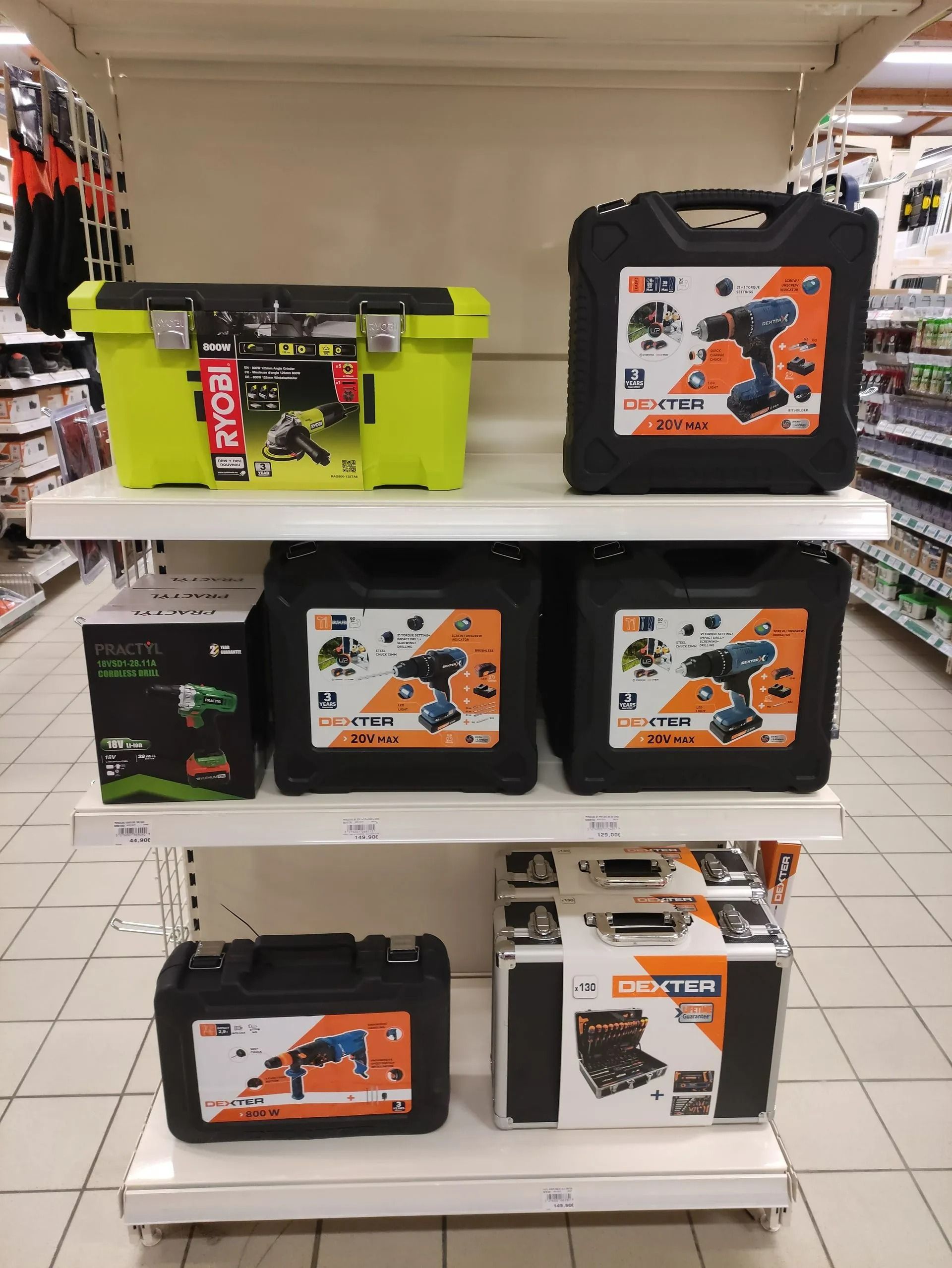 Rayon d'outils électriques et de coffrets dans une allée de magasin, avec des perceuses dans des boîtes orange et noires et une boîte à outils vert fluo