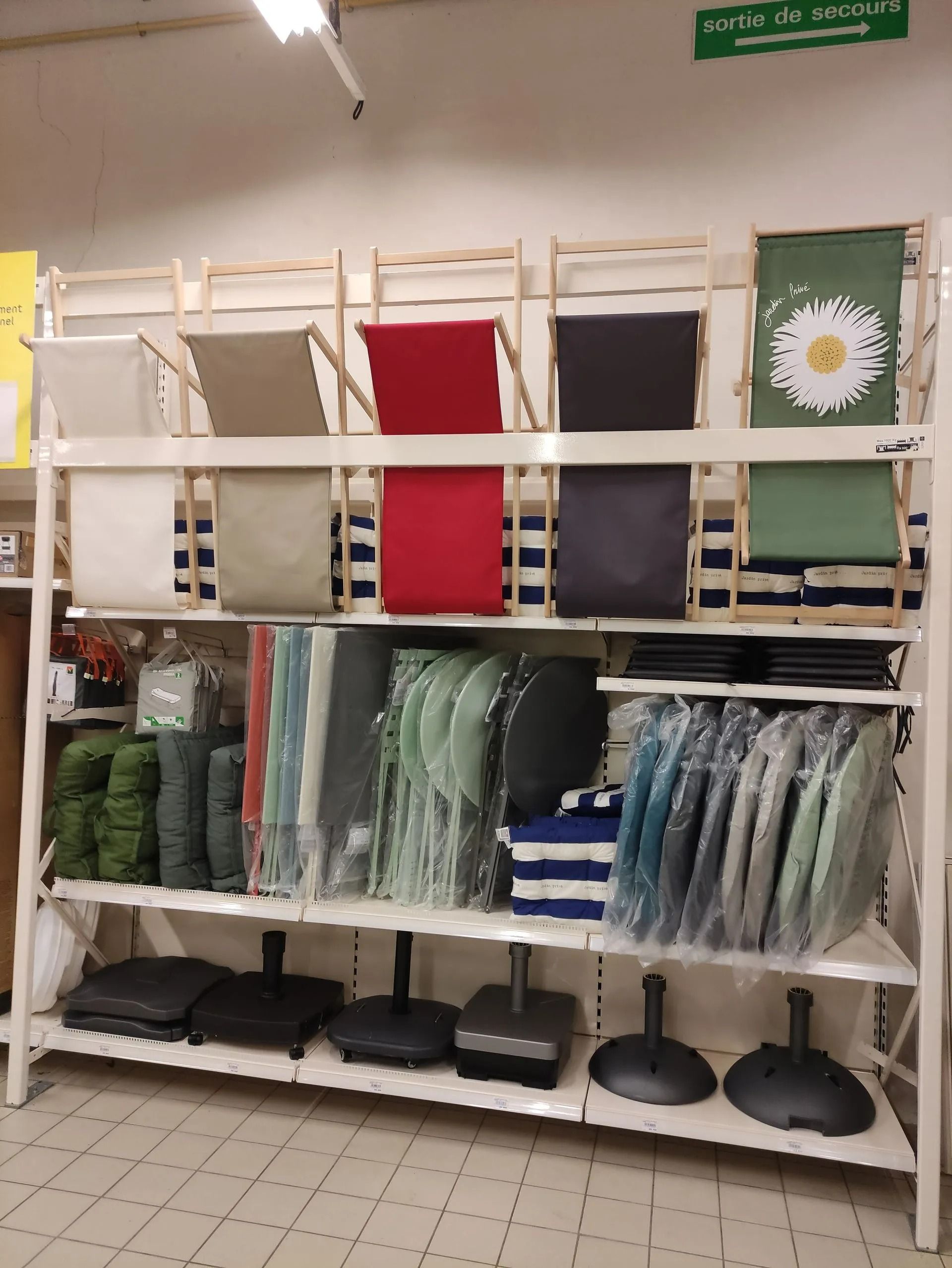 Étagère de rangement avec chaises de camping pliées, coussins et autres équipements de plein air pliés dans un magasin.