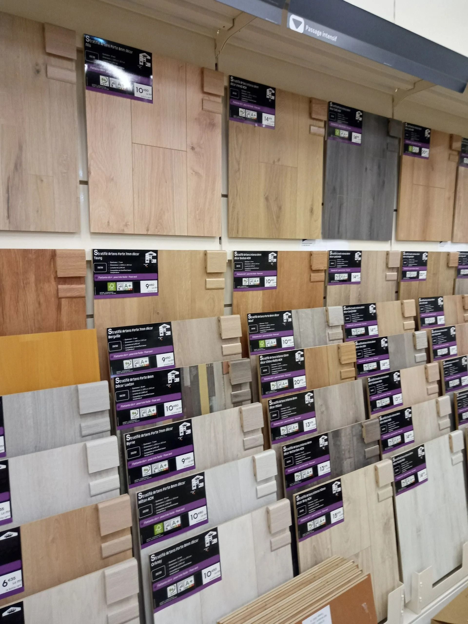 Présentation d'échantillons de parquets assortis dans un magasin, disposés en rangées sur des étagères murales