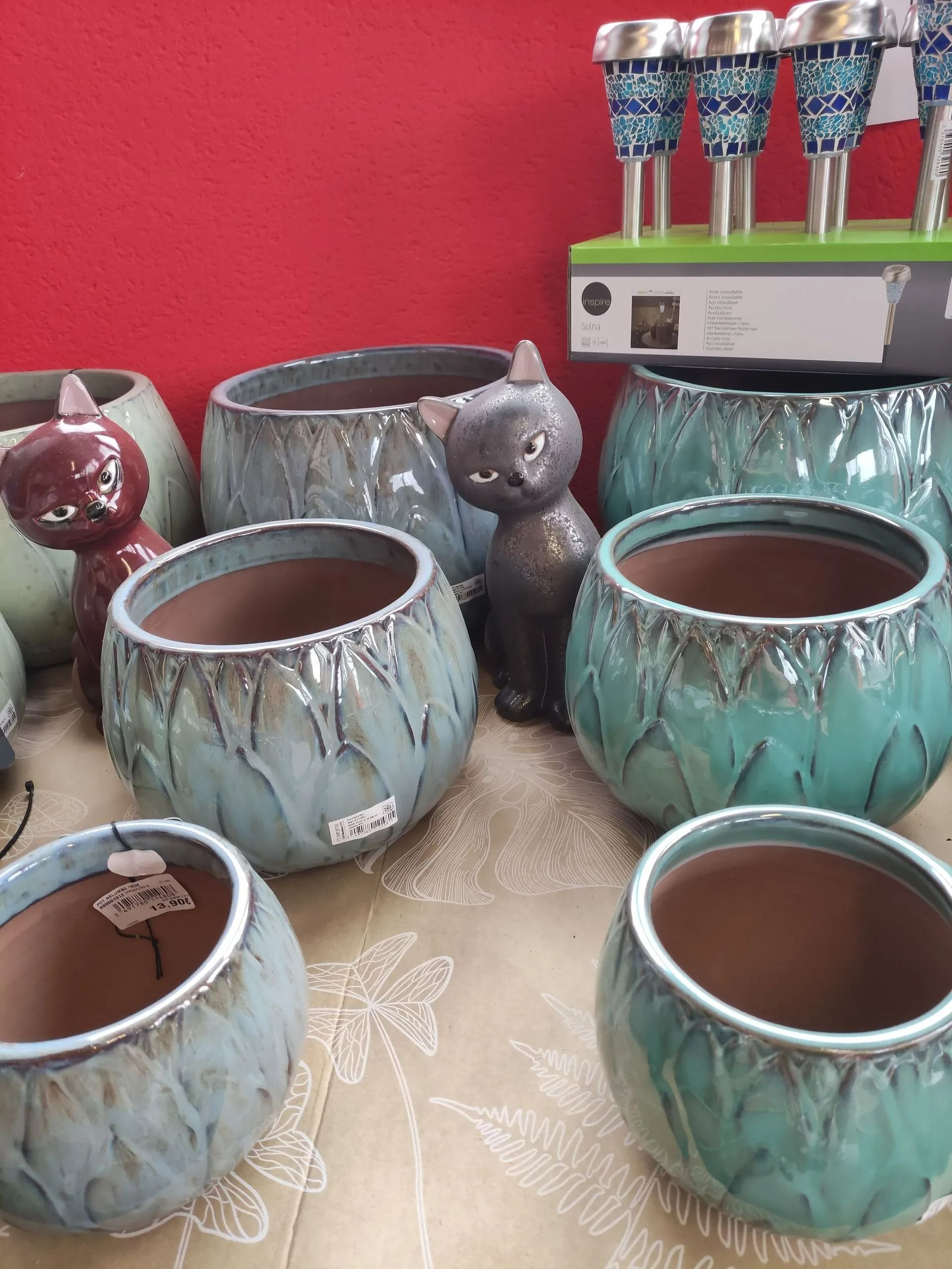 Des pots de fleurs en céramique et des figurines de chats sur une table, avec un fond rouge et un petit présentoir derrière.
