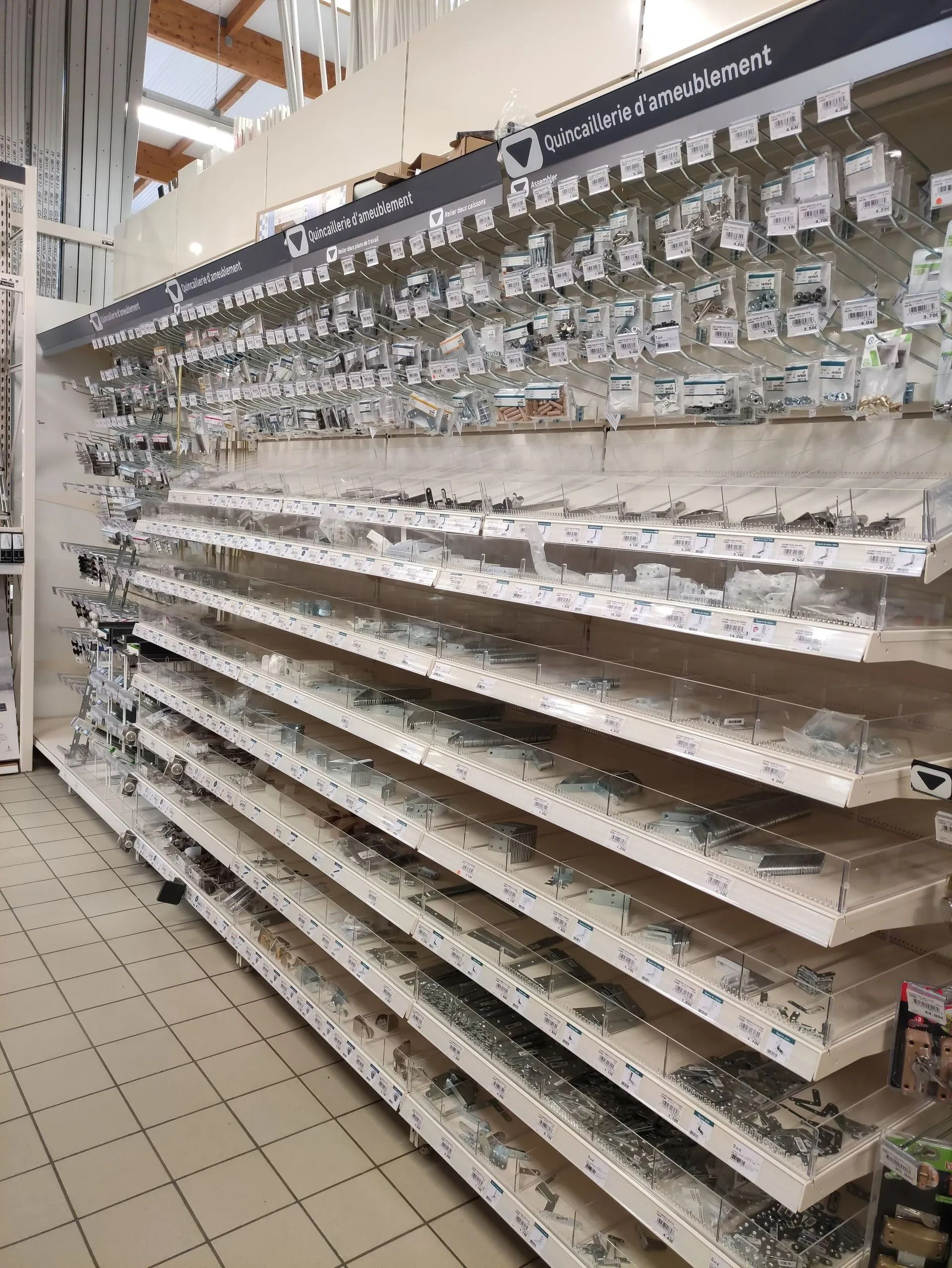 Rayons vides d'un magasin, avec des rangées de petits articles emballés et des étiquettes de prix dans une allée.