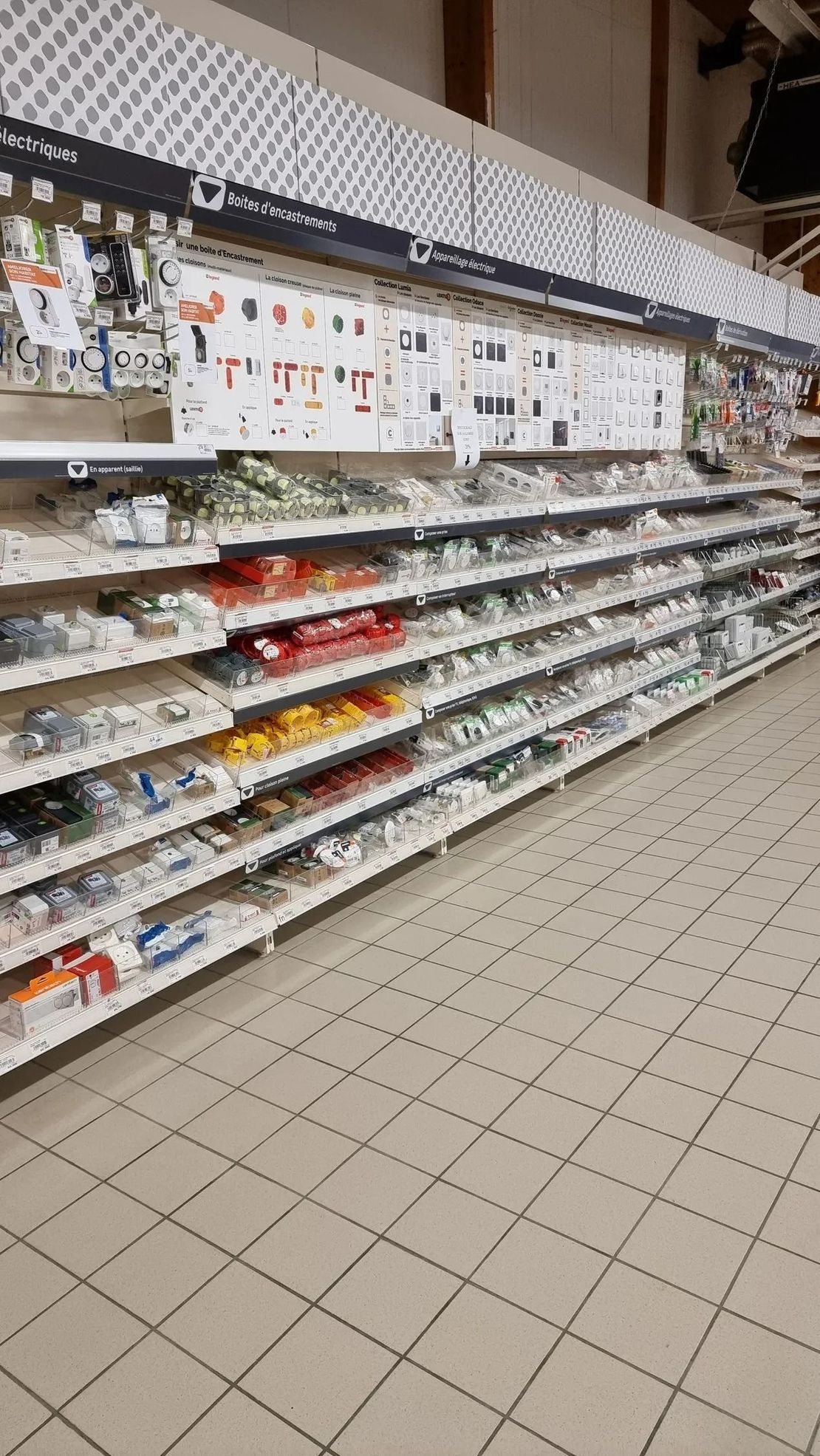 Une longue allée de magasin aux étagères pour la plupart vides, présentant de petits articles et des panneaux.