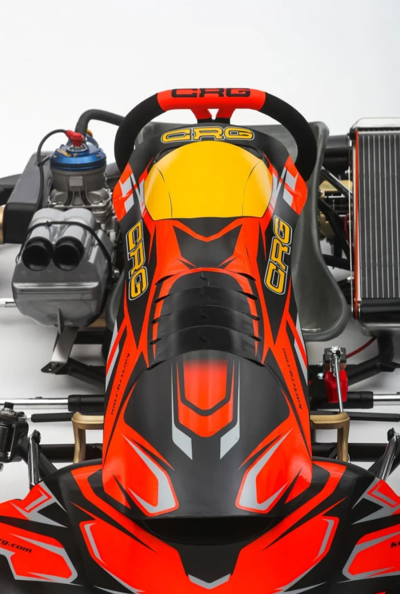 Ylhäältä alas katsottuna puna-mustan karting-ohjaamon, jossa on keltainen kypärä ja näkyvät moottorin osat