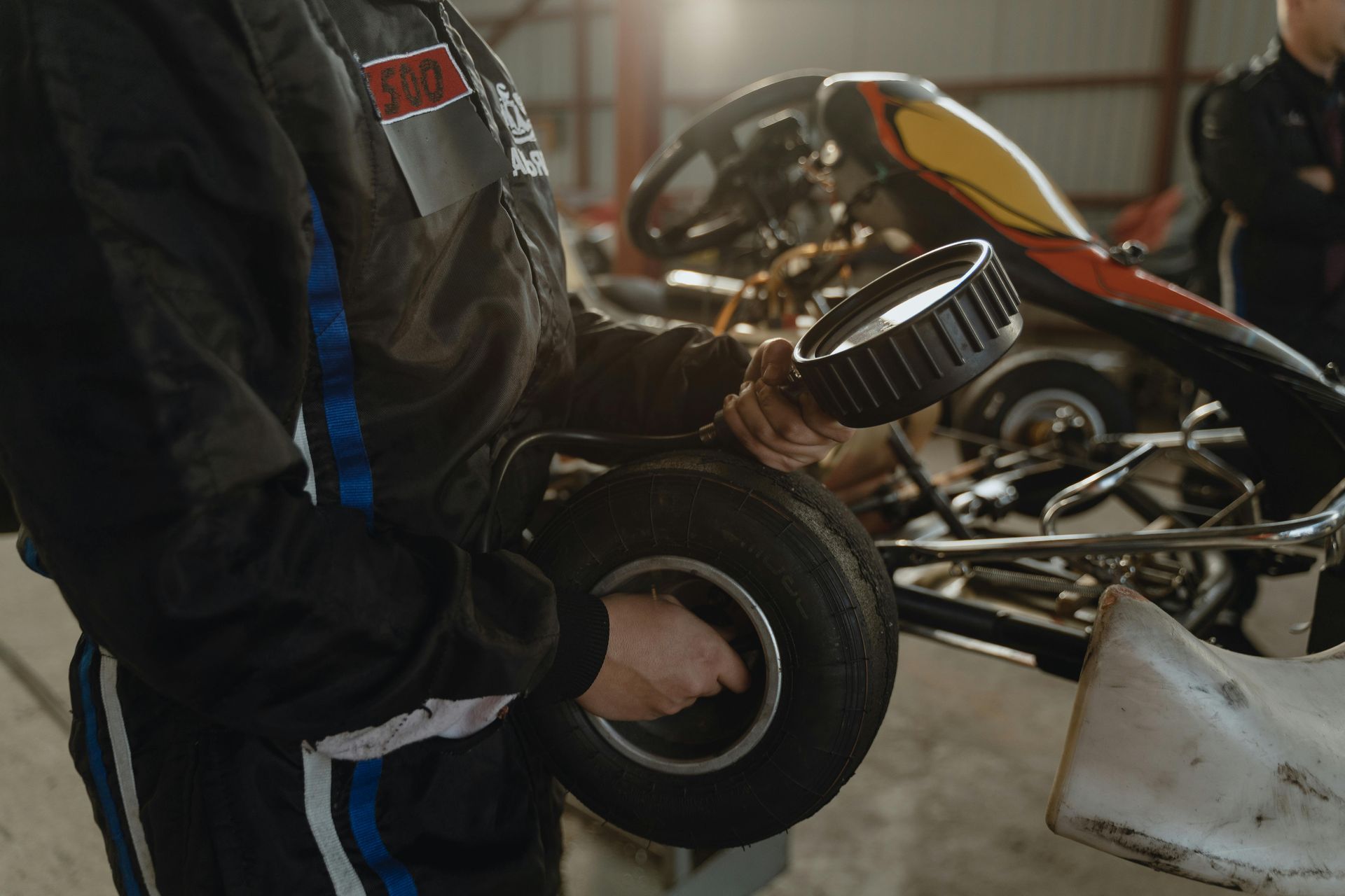 Mustassa kilpa-asussa oleva henkilö pitelee rengasta karting-auton vieressä autotallissa