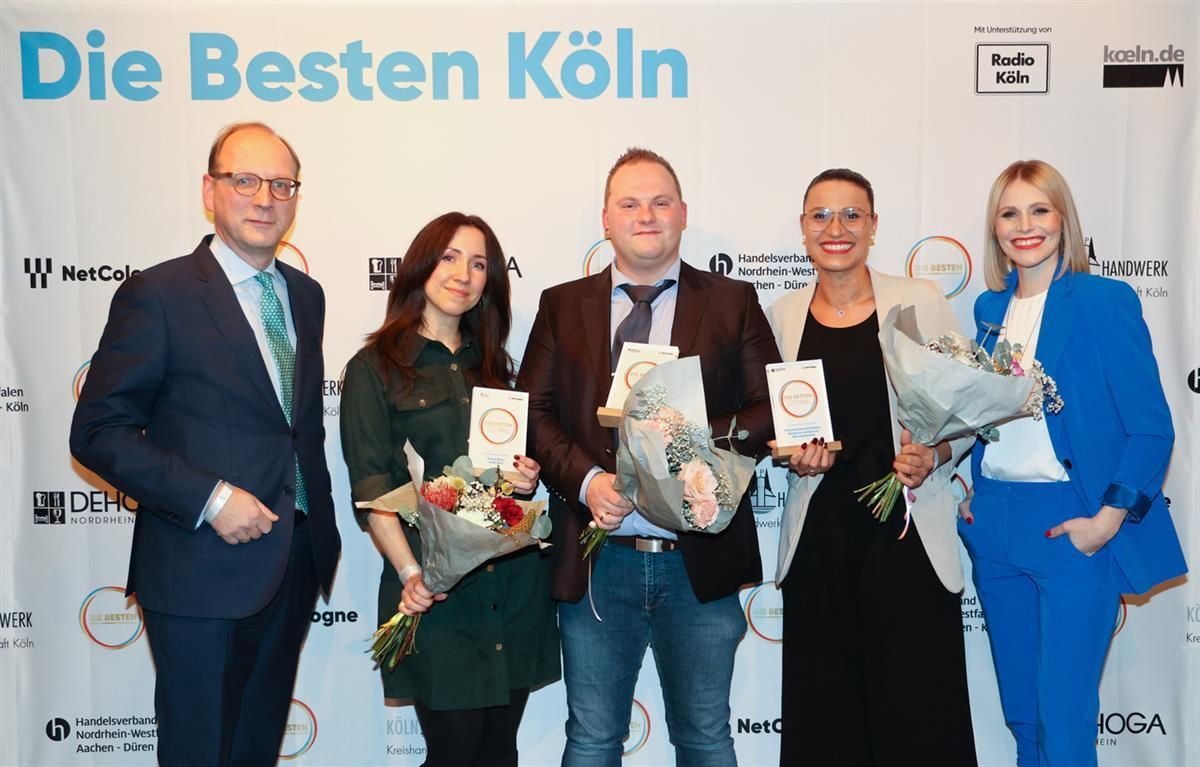 Eine Gruppe von Menschen steht vor einer Wand mit der Aufschrift „Die besten Köln“