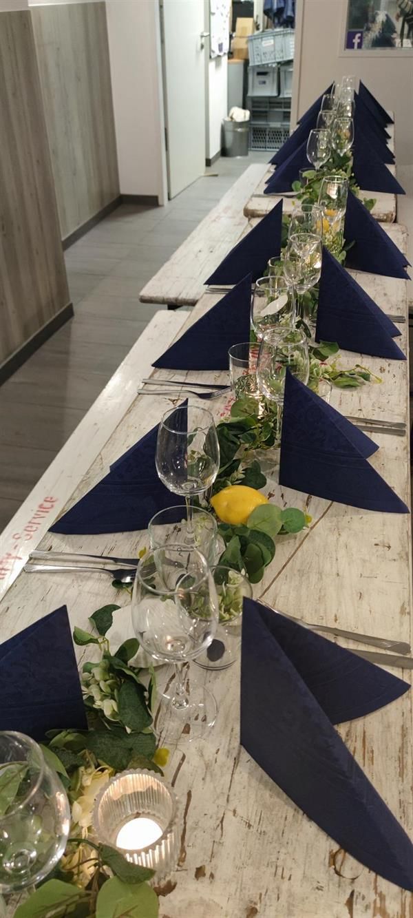 Ein langer Tisch mit blauen Servietten, Gläsern und Kerzen.