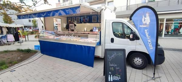 Ein weißer Lastwagen mit blauer Markise parkt neben einem Schild.