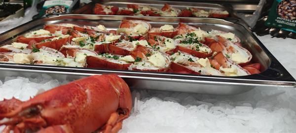 Ein Hummer liegt neben einem Tablett mit Hummern auf Eis.