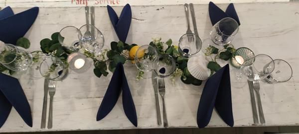 Ein Tisch mit blauen Servietten, Besteck und Gläsern darauf.