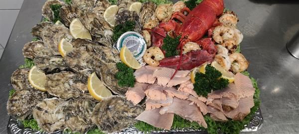 Ein Tablett mit Meeresfrüchten, darunter Austern, Hummer, Lachs und Schinken, auf einem Tisch.