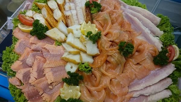 Ein Tablett mit geräuchertem Lachs, Fisch und Salat auf einem Tisch.