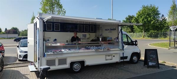 Ein Mann steht auf einem Parkplatz vor einem Imbisswagen.