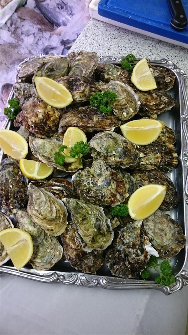 Ein Tablett mit Austern, Zitronenscheiben und Petersilie auf einem Tisch.
