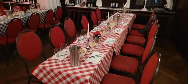 Ein langer Tisch mit einer rot-weiß karierten Tischdecke und roten Stühlen.