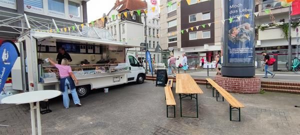 Auf einem Parkplatz steht ein Imbisswagen mit Tischen und Bänken.