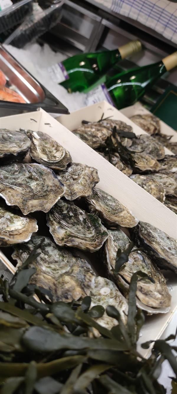 Eine Kiste Austern steht neben Weinflaschen auf einem Tisch.