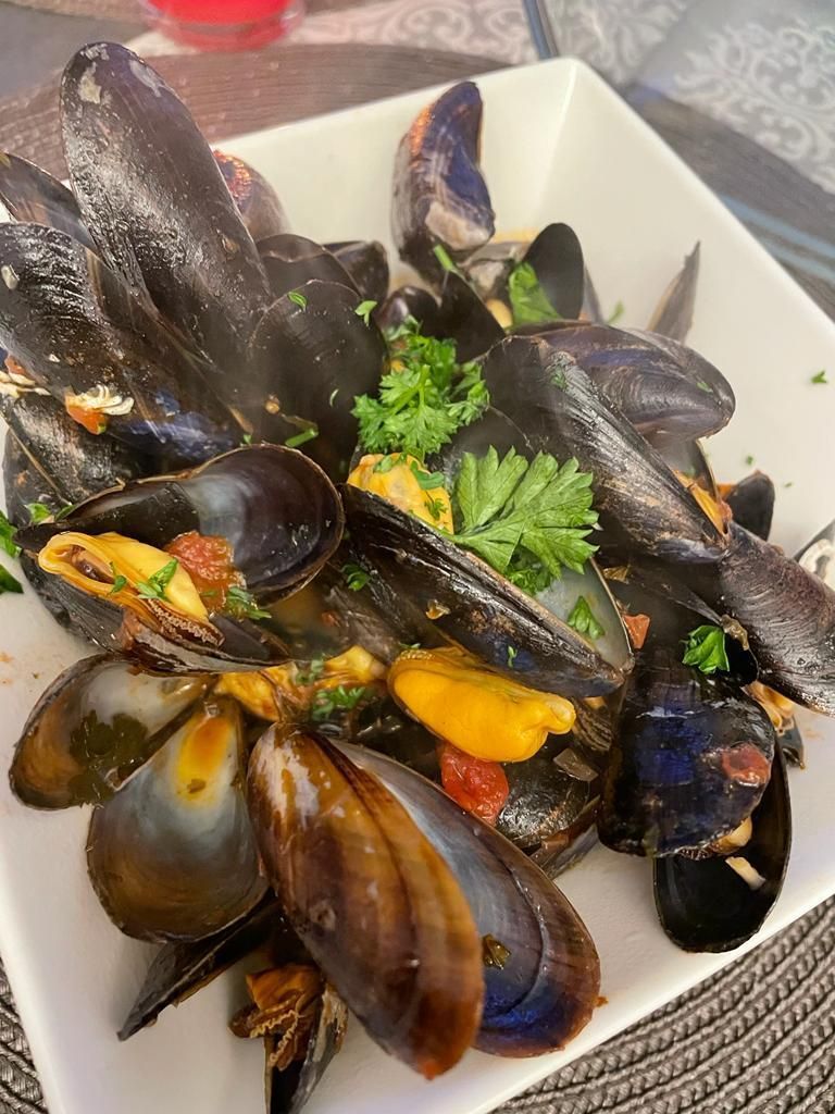 Ein weißer Teller mit Muscheln und Petersilie auf einem Tisch.