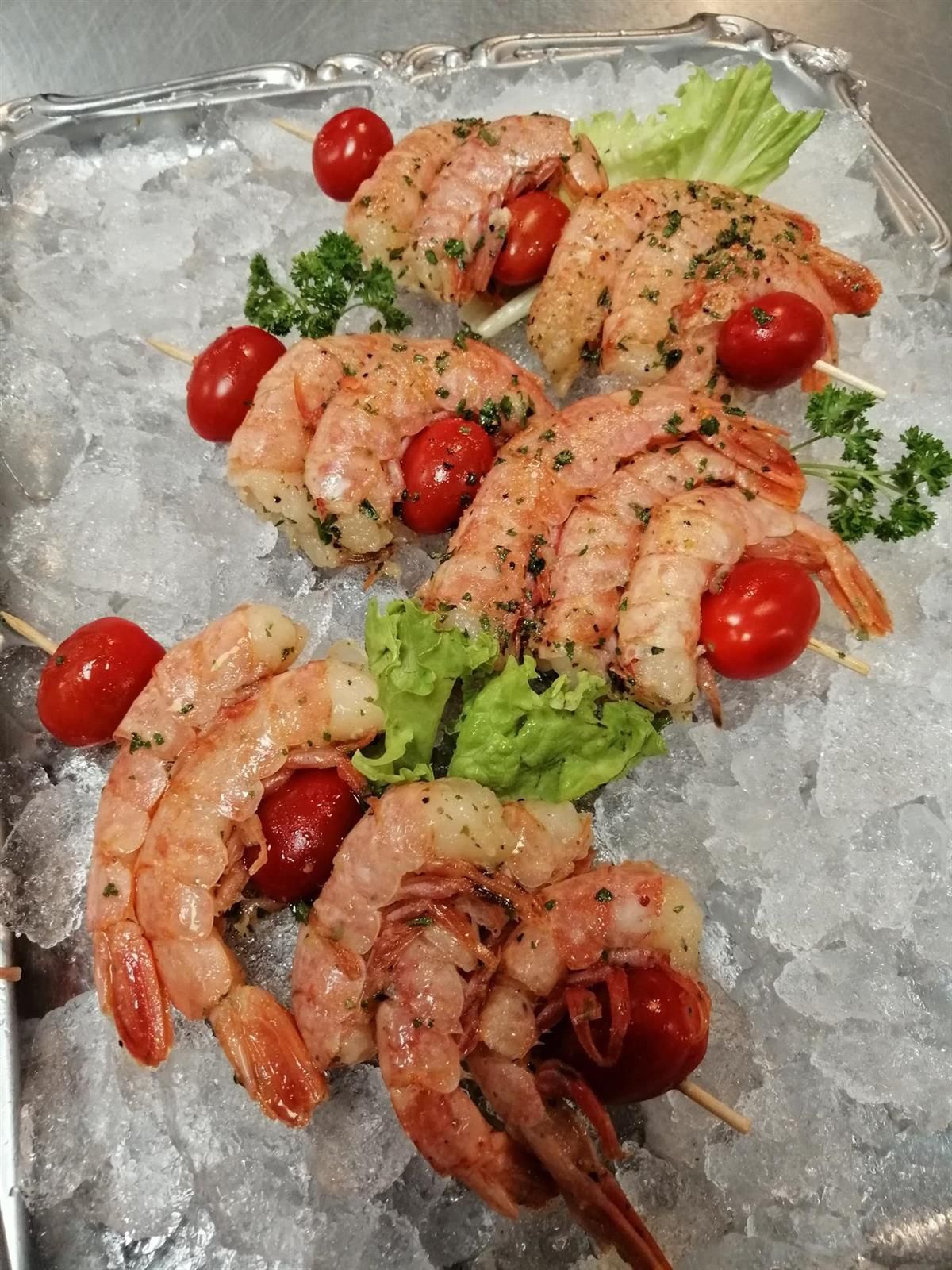 Garnelenspieße mit Tomaten und Salat auf Eis