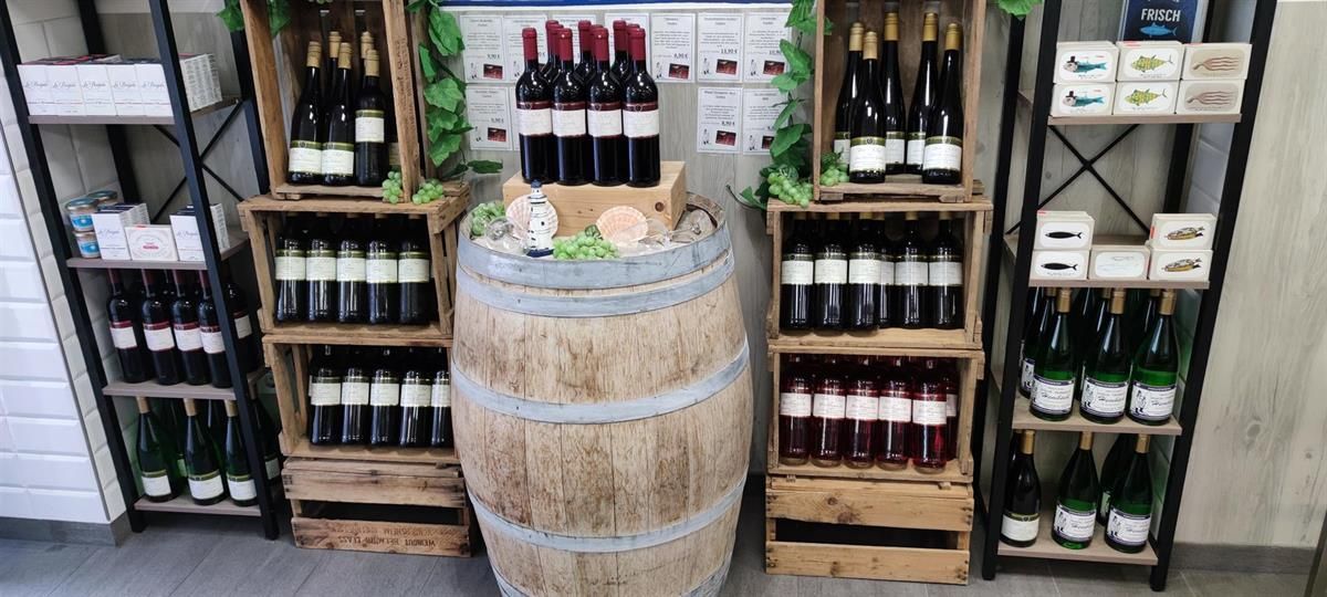 Vor einer Ausstellung mit Weinflaschen steht ein Holzfass.