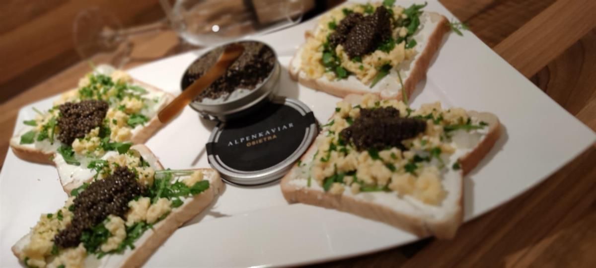 Ein weißer Teller mit Sandwiches und Kaviar auf einem Holztisch.