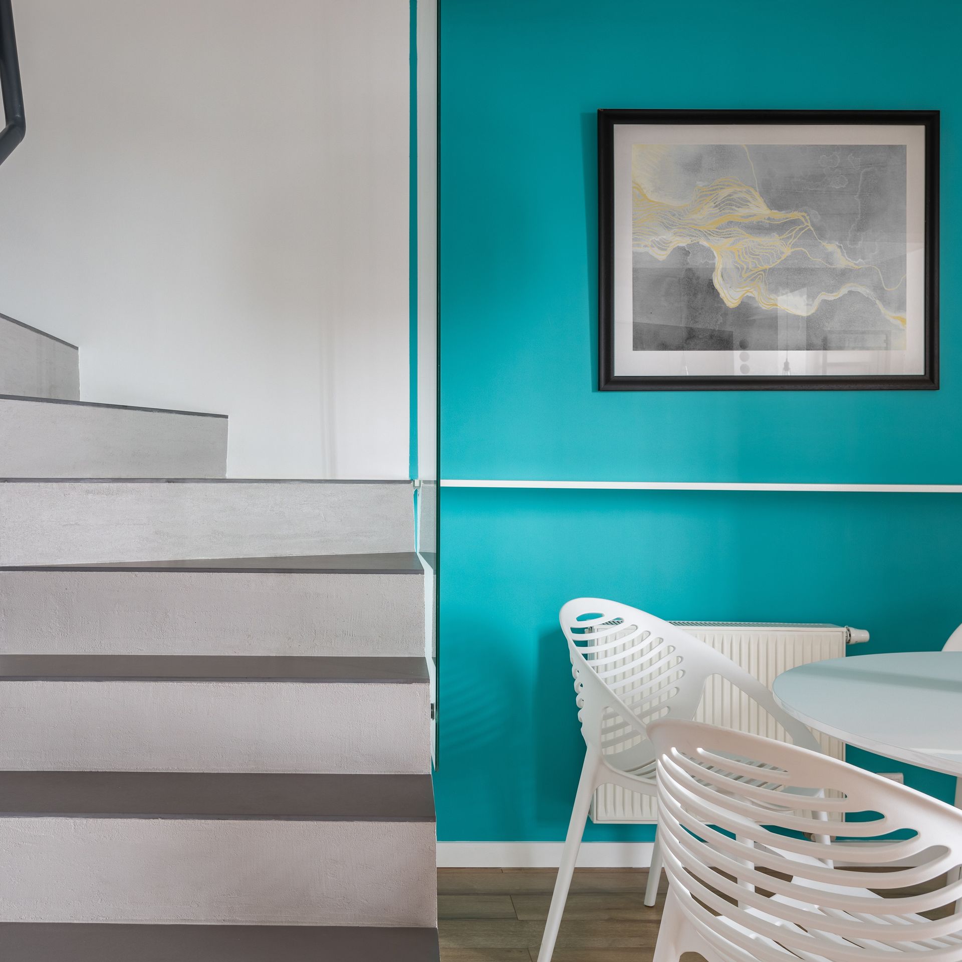 Un cuadro cuelga en una pared azul sobre una mesa y sillas.