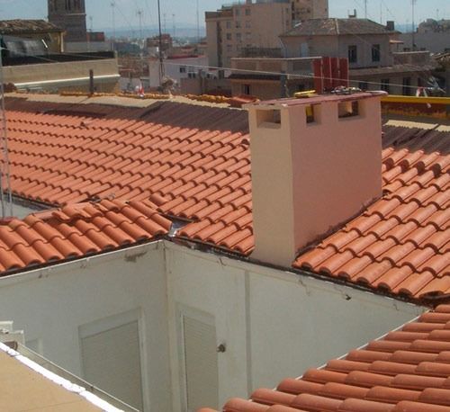 Un techo con tejas rojas y una chimenea encima.