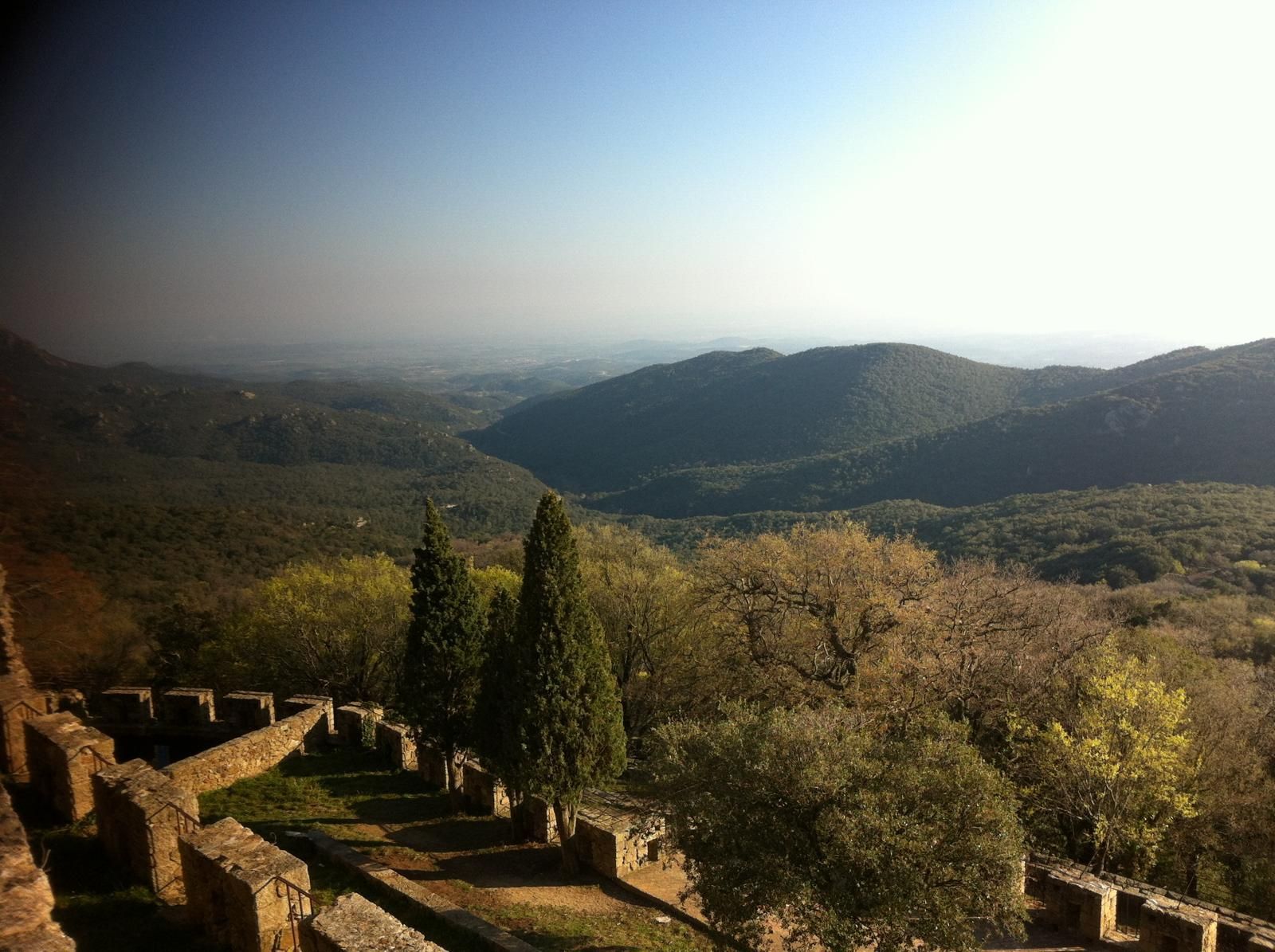 Vista de un valle desde una estructura de piedra. Paisaje montañoso, árboles y cielo azul. Día soleado.