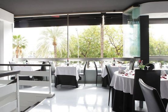 Comedor luminoso y moderno con manteles blancos y grandes ventanales con vistas a las palmeras.