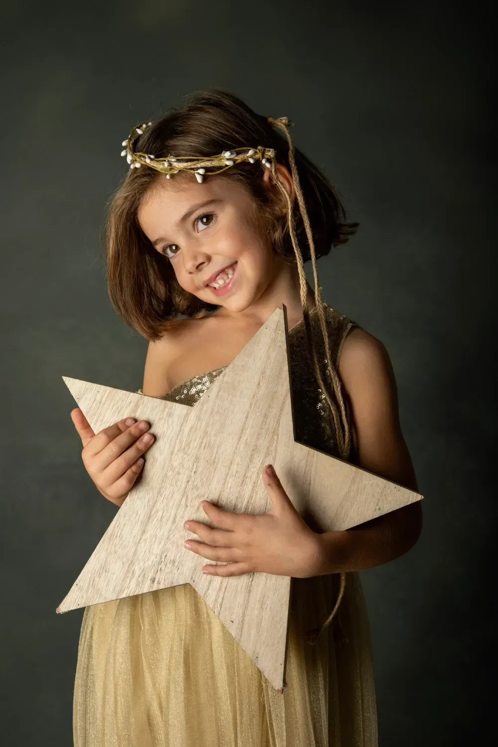 Niña con vestido dorado y estrella, sonriente, con tocado.