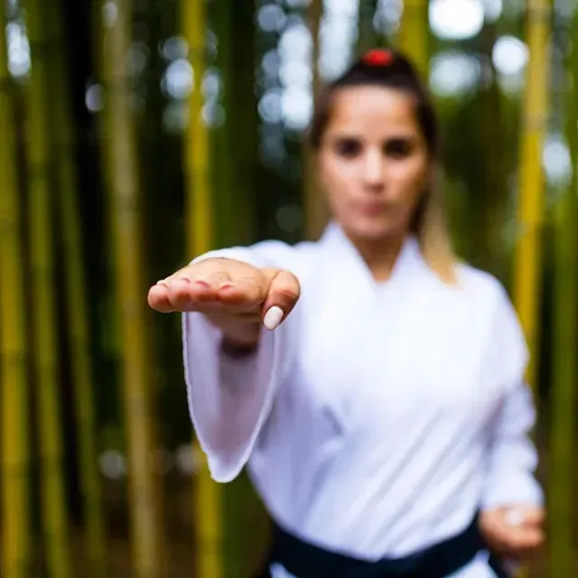 Una mujer con un uniforme de karate blanco está parada en un bosque.