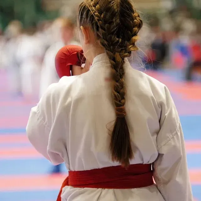 Una mujer con uniforme de karate lleva guantes rojos y una trenza.