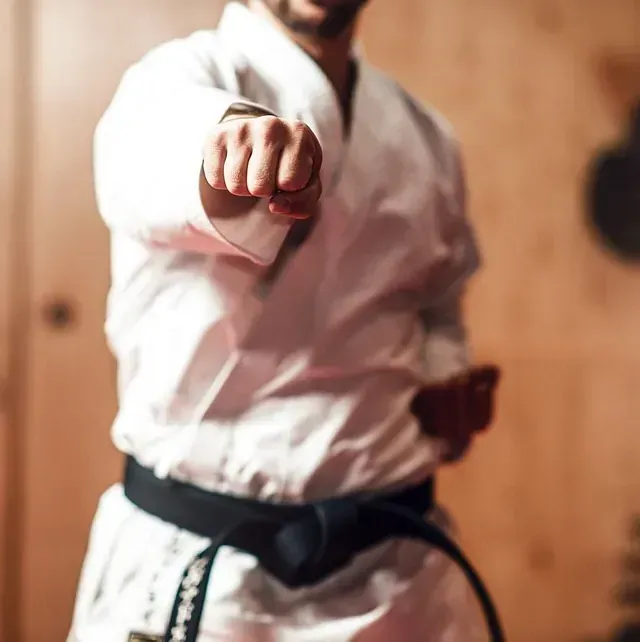 Un hombre con un uniforme de karate blanco apunta a la cámara.