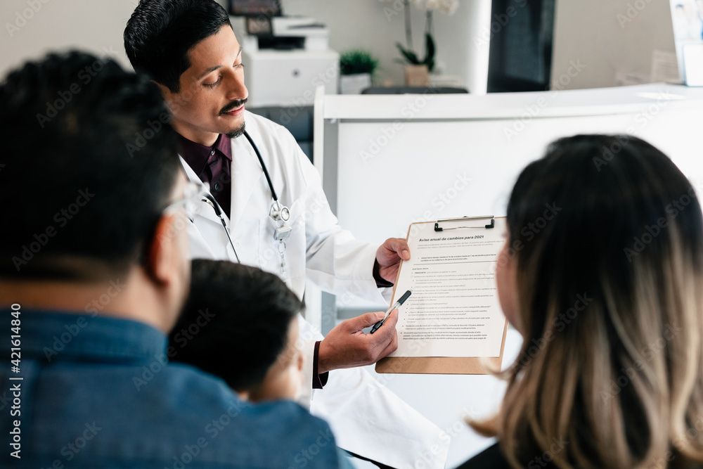 Un médecin montre un bloc-notes à des patients assis dans une salle de consultation.
