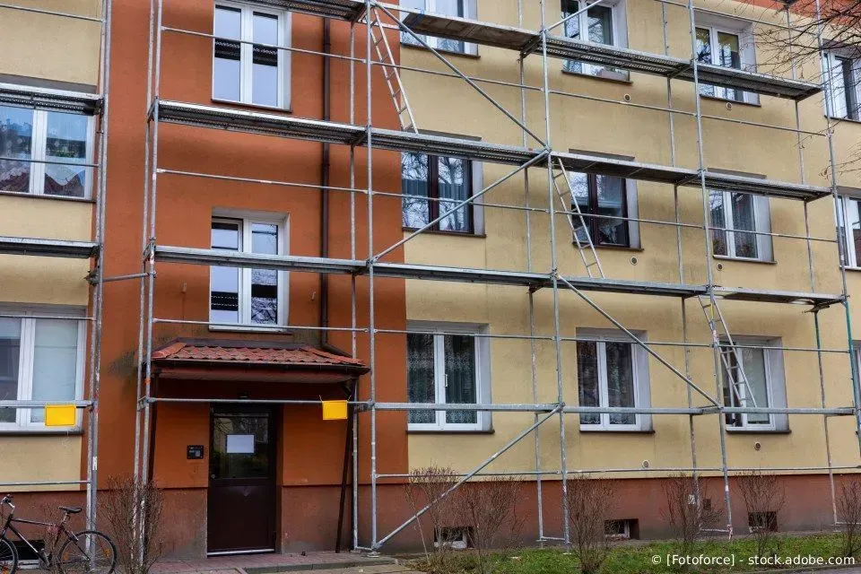 Gerüst an der Fassade eines orangefarbenen Wohnhauses mit Fenstern und einer braunen Eingangstür