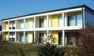 Zweistöckiges, modernes Mehrfamilienhaus mit weißen und gelben Balkonen in einem sonnigen Wohngebiet