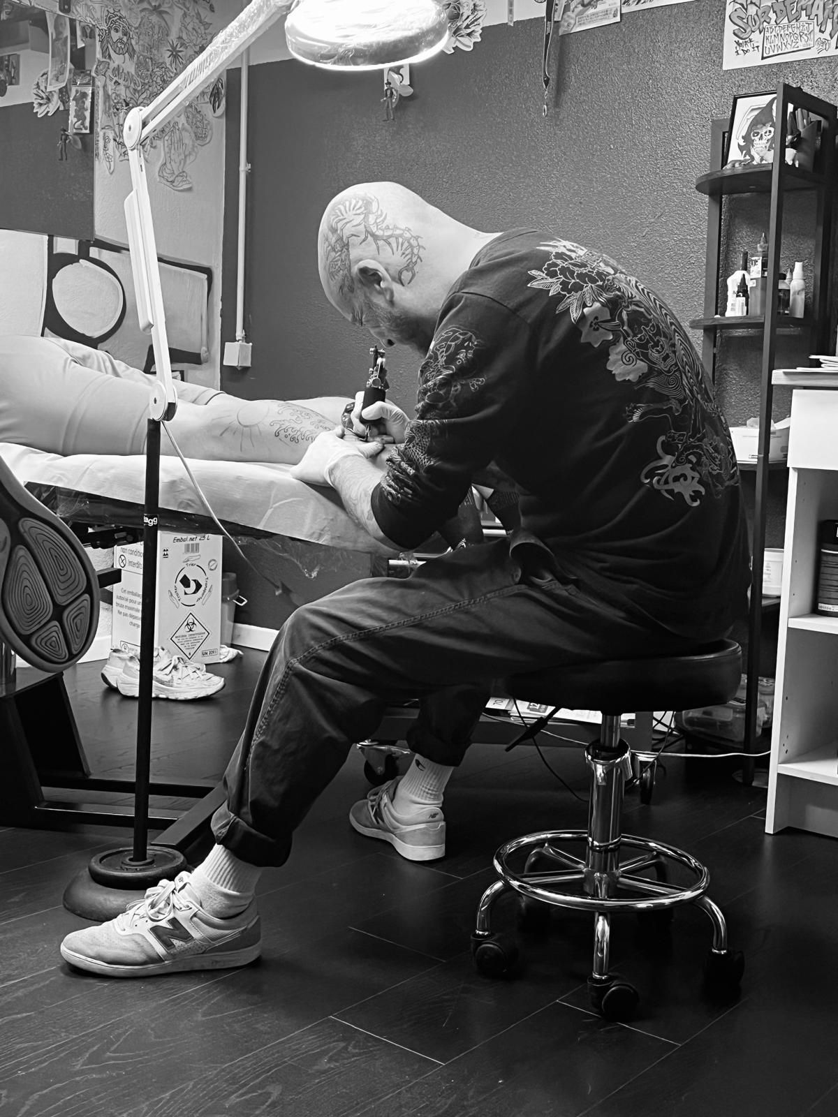 Une photo en noir et blanc d'un homme qui tatoue un mollet