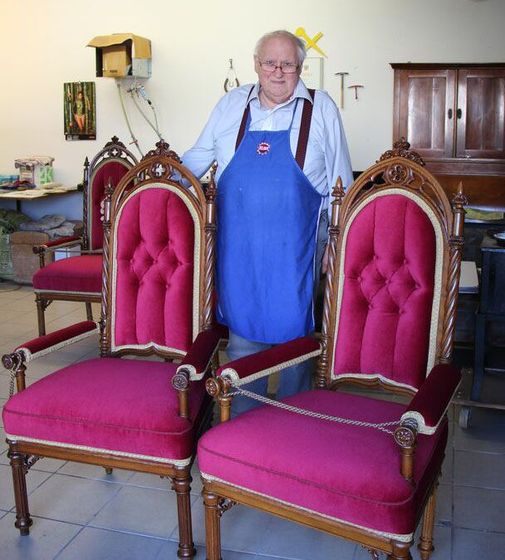 Ein Mann in einer blauen Schürze steht zwischen zwei rosa Stühlen