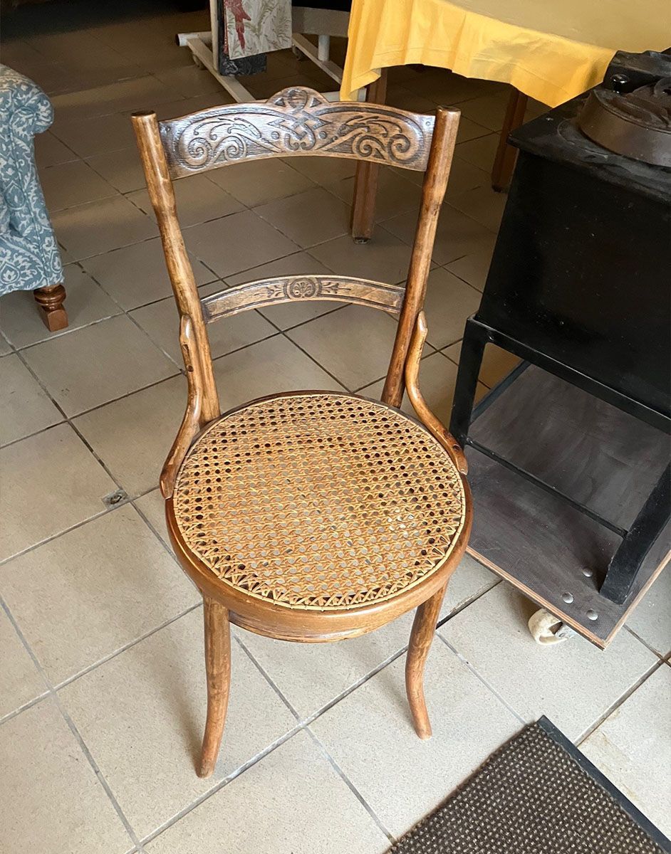 Auf einem gefliesten Boden steht ein Holzstuhl mit einer Sitzfläche aus Korbgeflecht.