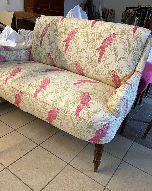 Auf einem gefliesten Boden steht ein weißes Sofa mit rosa Vögeln darauf.