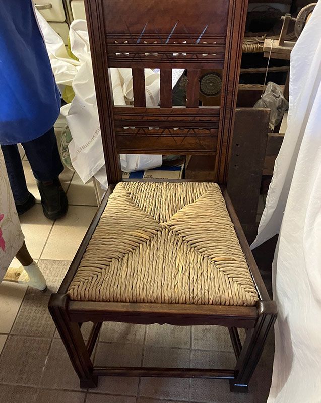 In einem Raum steht ein Holzstuhl mit einer Sitzfläche aus Korbgeflecht.