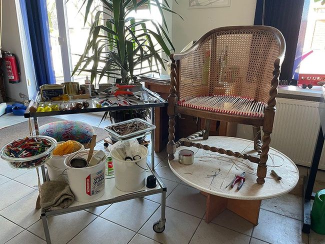 In einem Raum steht ein Korbstuhl auf einem weißen Tisch.