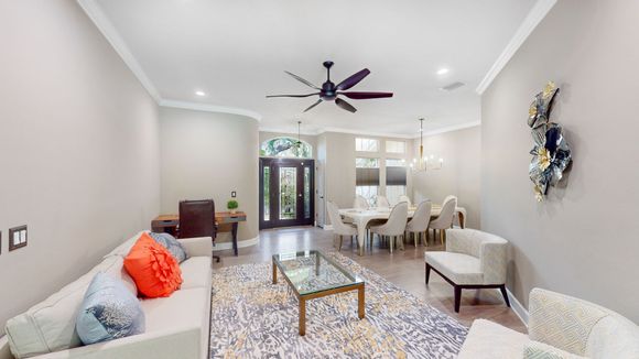 Spacious living room with white sofa, patterned rug, and dining area. Features neutral walls, wooden floors, and a large ceiling fan.