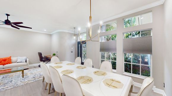 Elegant dining room with a long table set for guests, cream chairs, and large windows overlooking greenery.